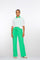 "Woman wearing a summery outfit featuring a sheer white short-sleeved sweater layered over a green polo shirt, paired with bright green wide-leg trousers with a tie waist and beige sandals."